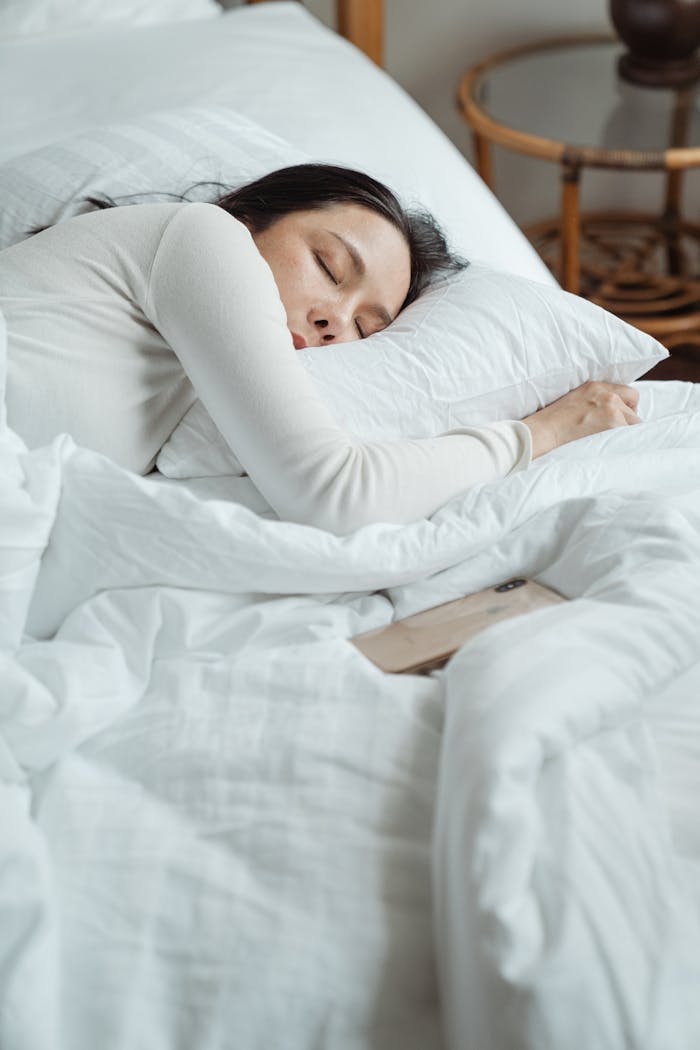 services-06 Woman in a cozy bedroom sleeping peacefully, surrounded by white bedding for ultimate comfort.