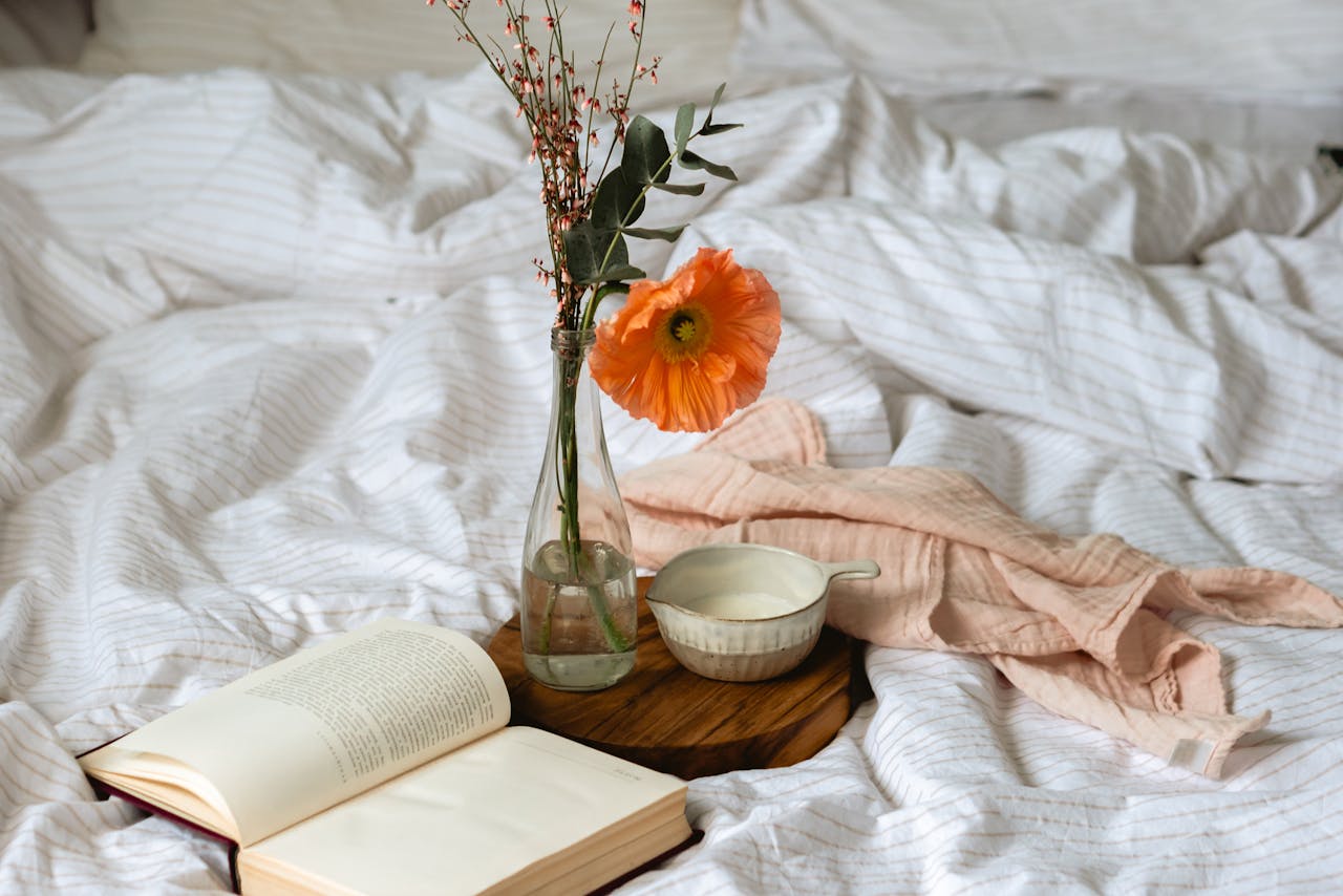 A peaceful bedroom scene with an open book, vase with flowers, and a cup on a wooden board.