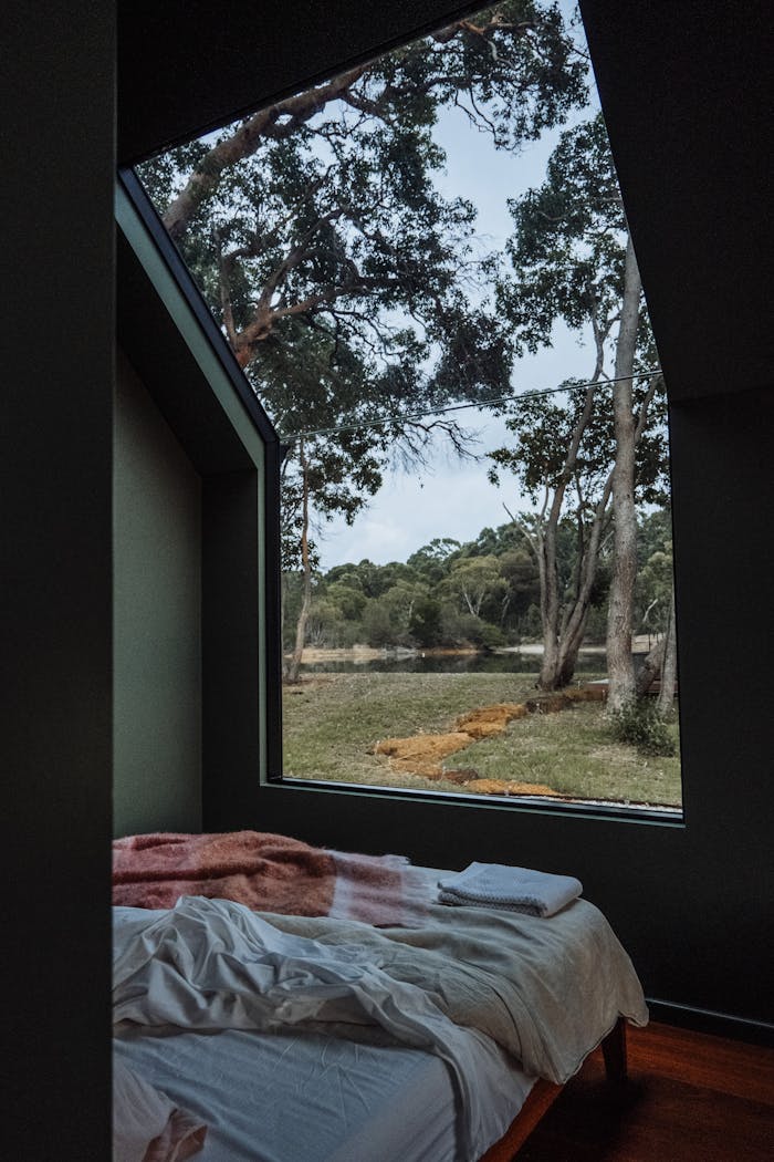 A cozy bed by a large window overlooking a serene forest landscape, perfect for relaxation.